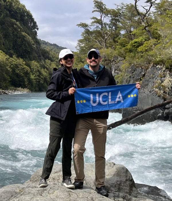 Alumni Travel - two travelers holding UCLA banner by river